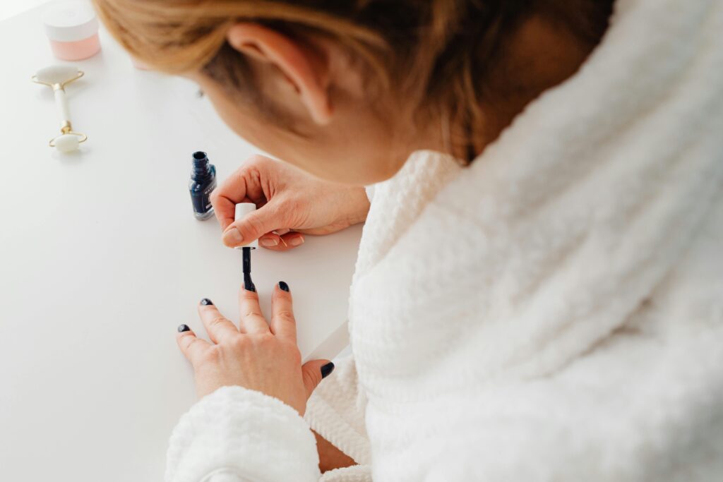 A woman in a bathrobe paints her nails indoors as part of a self-care routine.